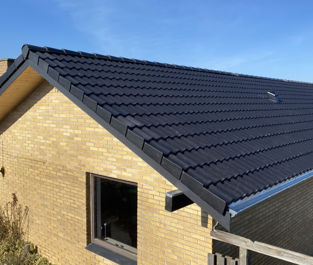 Sort tegltag på et gult murstenshus under blå himmel.